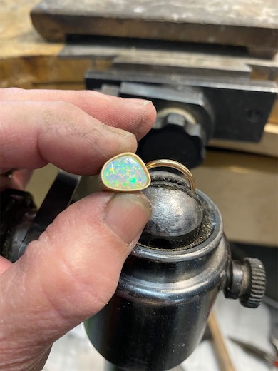 Hands holding a pale gemstone setting at a jeweler's bench